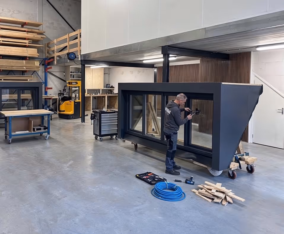 Man werkt aan dakraam in lichte werkplaats met houten planken en gereedschap op de vloer.