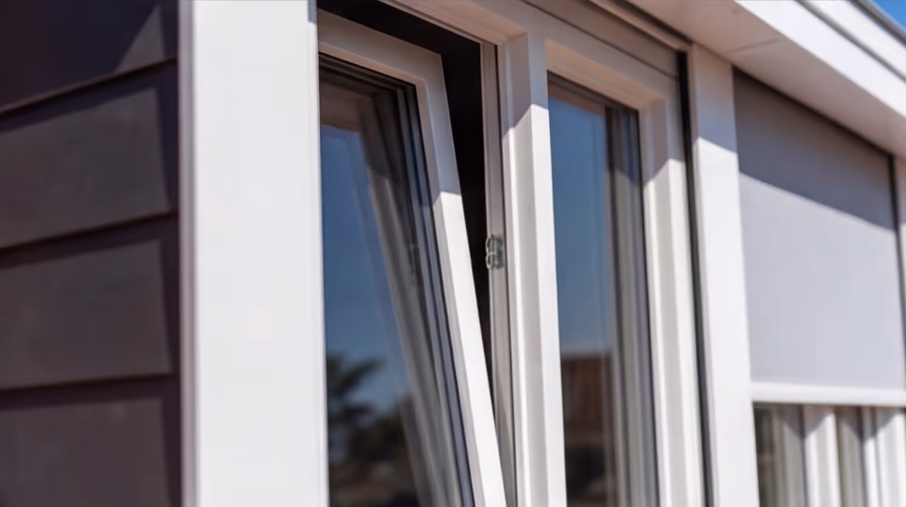 Open white kozijnraam met reflecties van buiten en een rolluik aan de rechterkant.