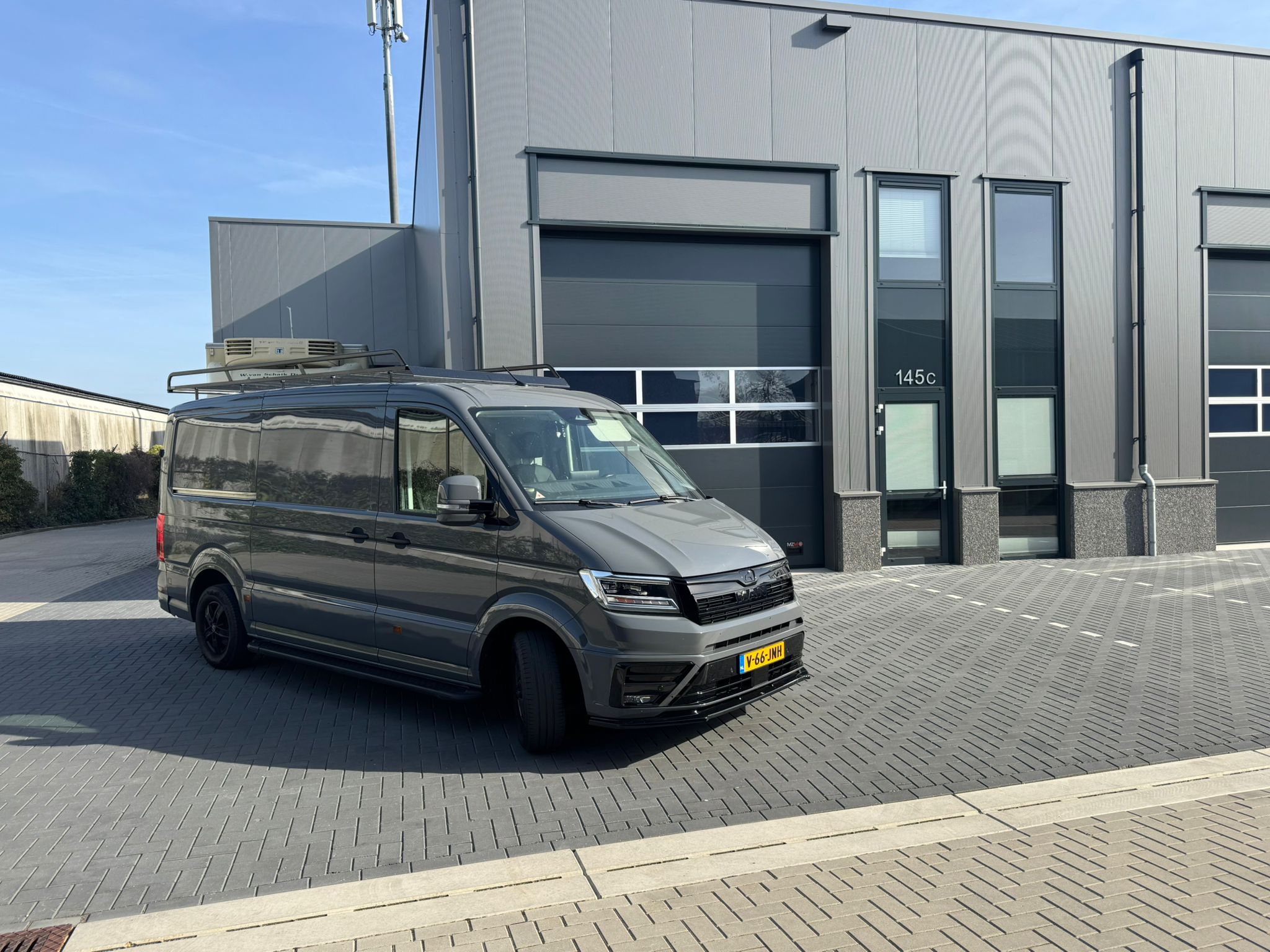 Grijze bestelbus geparkeerd voor een industrieel pand met nummer 145c op de deur.